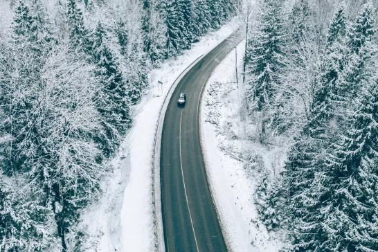 Aerial view of winter road with car and snow covered trees in the forest