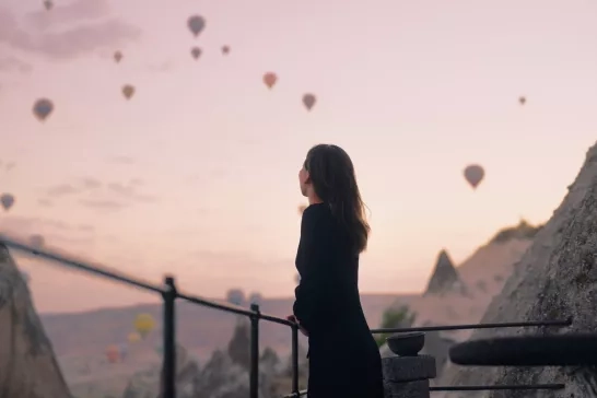 Female tourist enjoying watching hot air balloons flying in the sky at rooftop of hotel where she is staying during her vacation