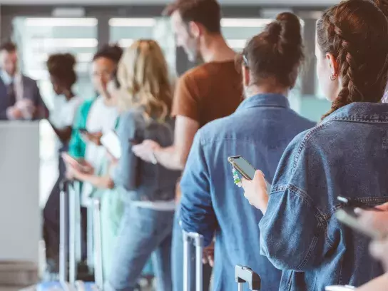 ravelers with luggage using smart phones while waiting in line for boarding at airport.