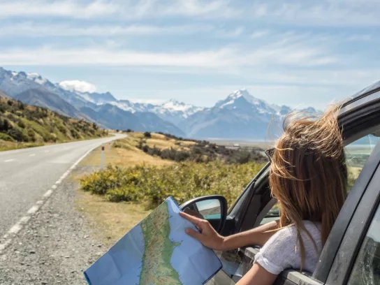 Portrait of a young woman in a car looking at a map for directions.