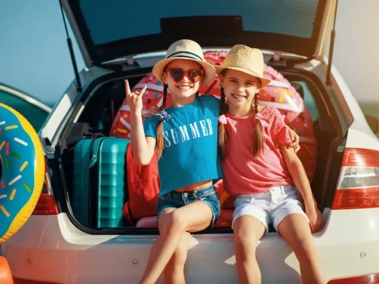 Two kids stting in open trunk of station wagon ready to go on a summer road trip