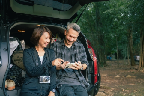 A couple using their phone by their packed car trunk in the forest