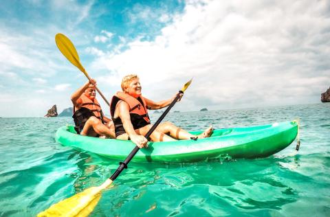 Happy retired couple enjoying travel moment paddling on kayak at Angthong marine park in Ko Samui in Thailand - Active elderly concept around world nature wonders - Bright vivid filtered tone