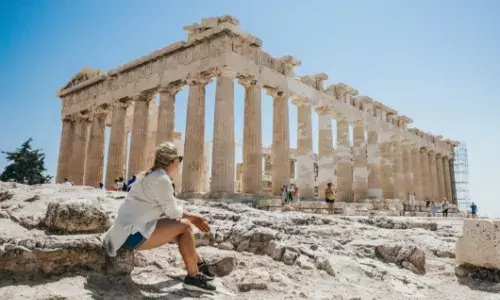 Woman siting on a rock beside the Parthenon Temple in Athens, Greece