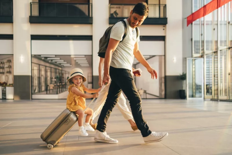 A father towing wheely luggage with child riding on top