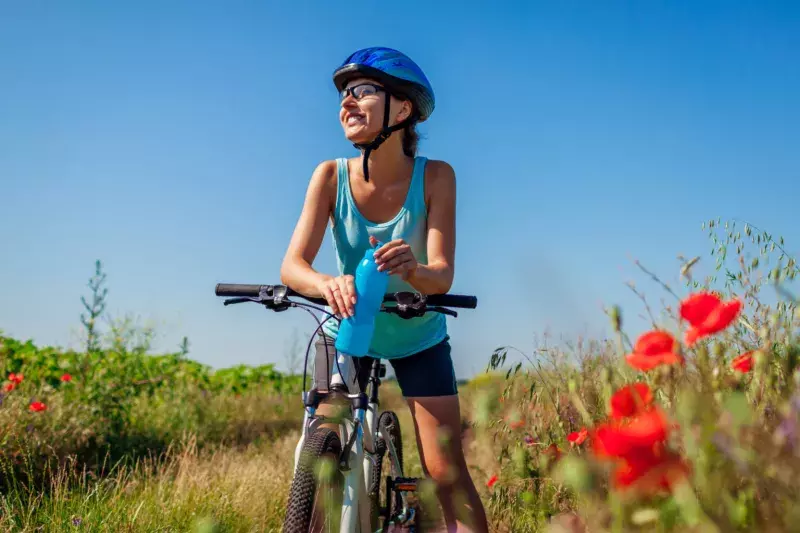 A woman pausing from a ride on a path to enjoy the view and have some water