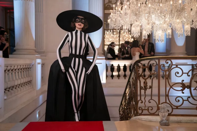 A woman in a vertical striped body suit and large hat ascending the top of a set of stairs