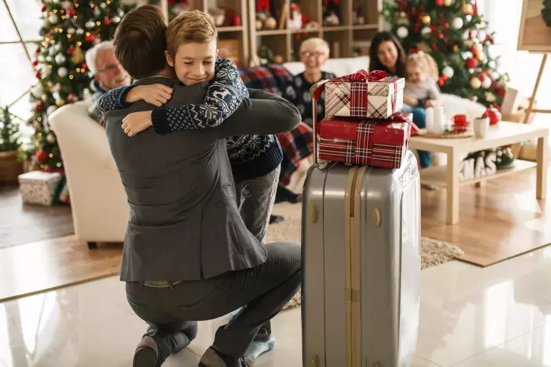  cheerful boy hugging his businessman father who just returned home with Christmas gifts