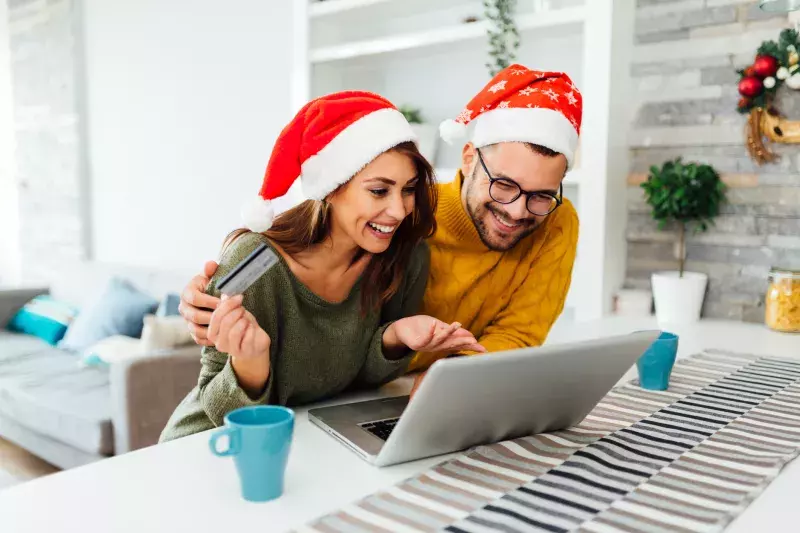 Young Caucasian lovers relaxing at home during winter holidays, having fun, shopping using a laptop and a credit card and smiling