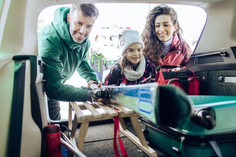 Happy family packing suitcase and sleigh into the car trunk and preparing for their winter vacation.