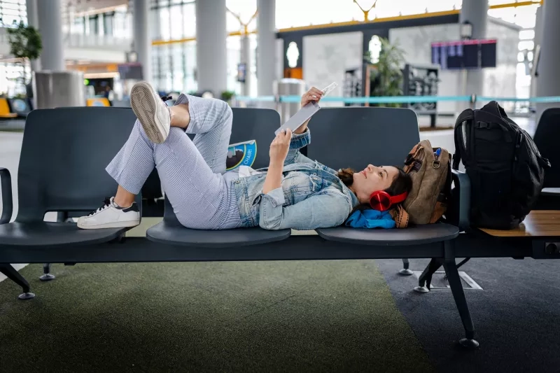 Young Woman waiting for delayed flight and reading digital book on chairs stock photo