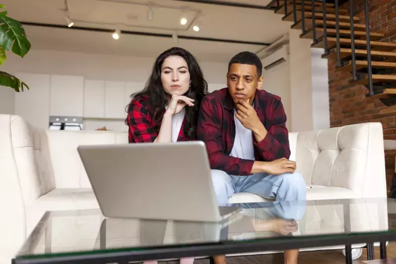 Young multiracial couple looking puzzled and serious at laptop on sofa, african american man with woman confused