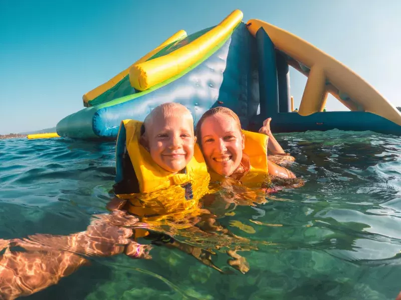 Mother and child wearing lifejackets in water at waterpark