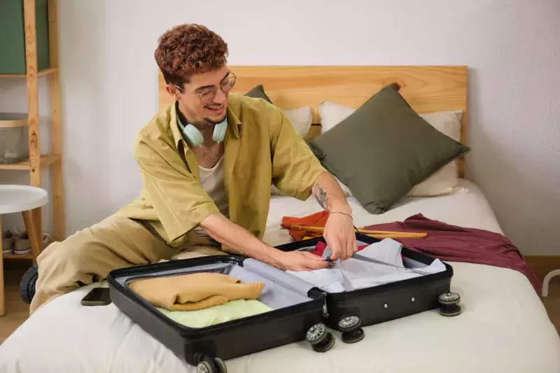 young man is packing his suitcase on a bed