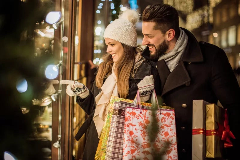 Young couple walking in downtown for Christmas. Holding Christmas gifts and big Teddy bear. Wearing warm clothing.