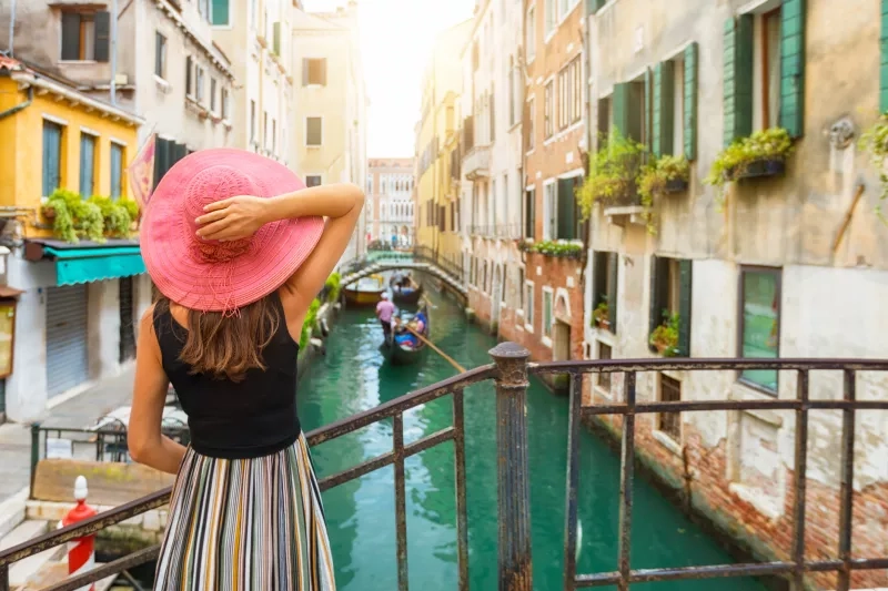 woman with red sunhat enjoys the view to a canal with passing by gondola in Venice, Italy