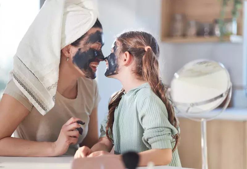 Cheerful girl smiling and embracing young woman with moisturizing mask.