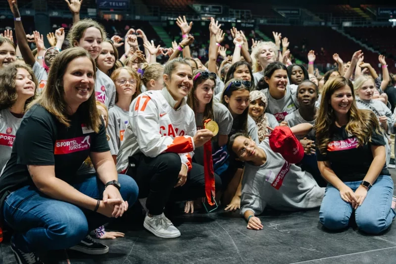 Olympic medalist showing off her medal surrounded by girls celebrating Sports Day the Girls Way