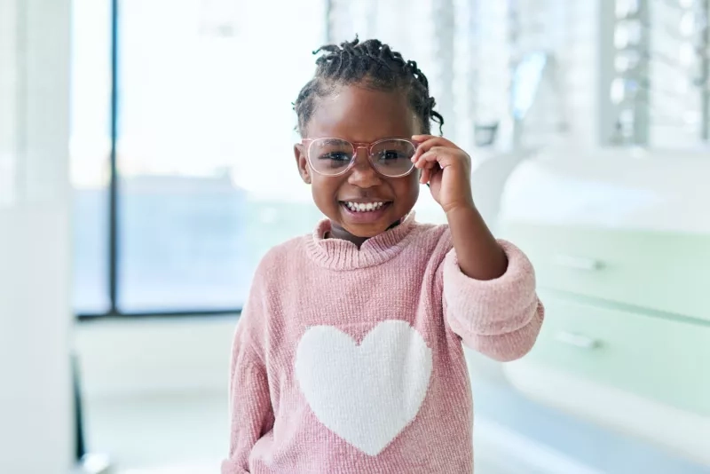 Young child, staring at camera, putting glasses on in the store