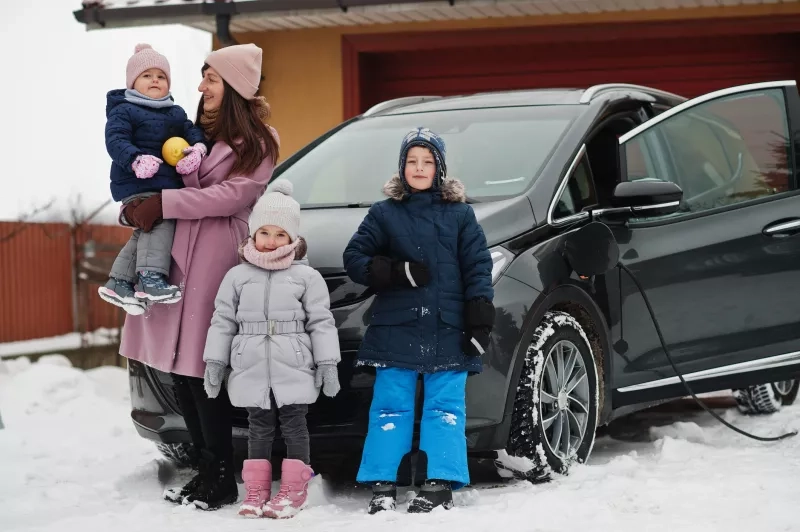 Young mother with kids charging electric car in the winter.