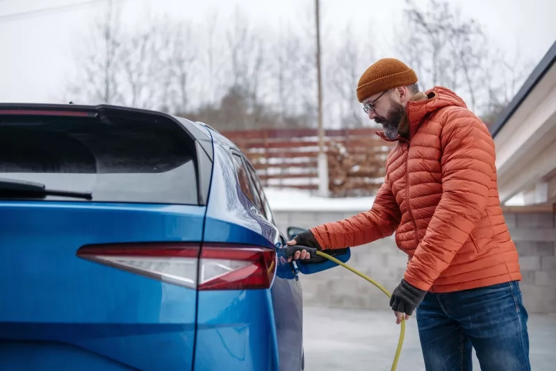 Man charging electric car during cold snowy day. 