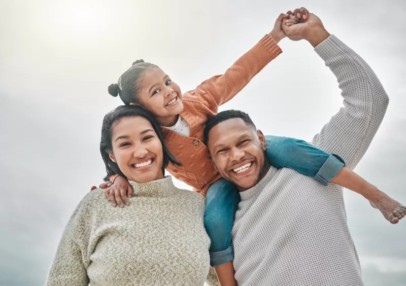 Kid sitting on father's shoulders, and leaning on mom