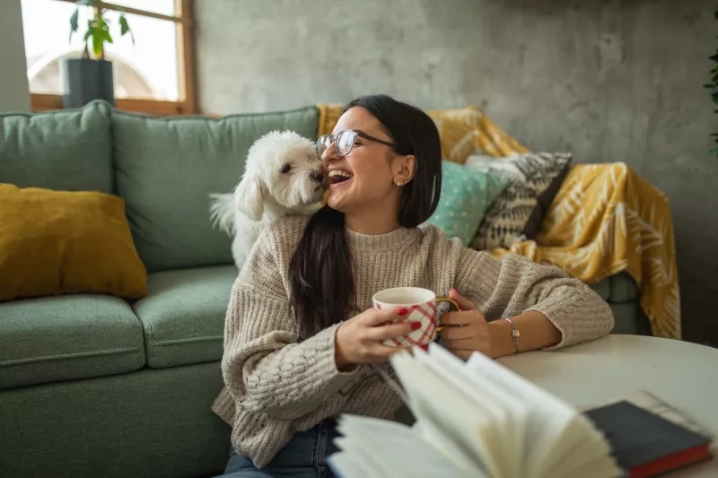 Young woman drinking tea while playing with her dog at home