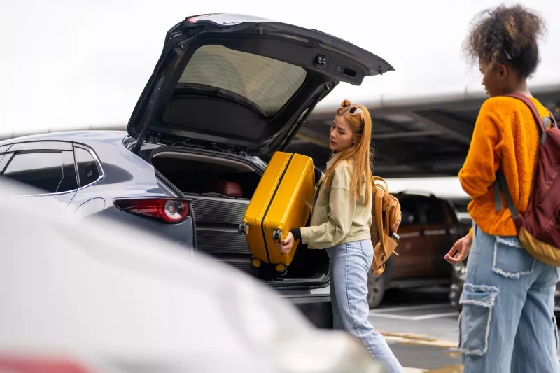 Women removing luggage from car trunk in airport parking