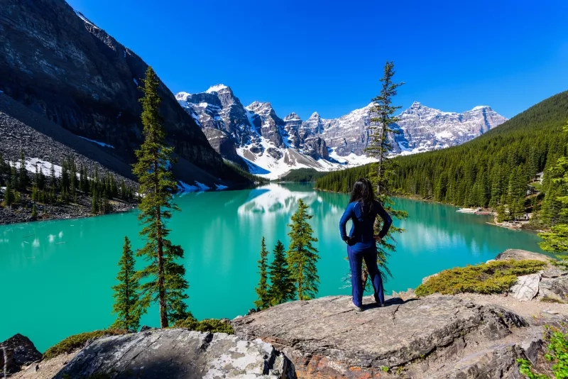 Woman on cliff admiring Moraine Lake and mountains scenic view, Rocky Mountains, Banff National Park, Alberta, Canada