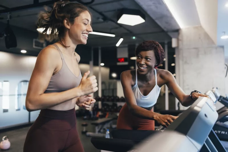 Two women running on a treadmill at the gym.