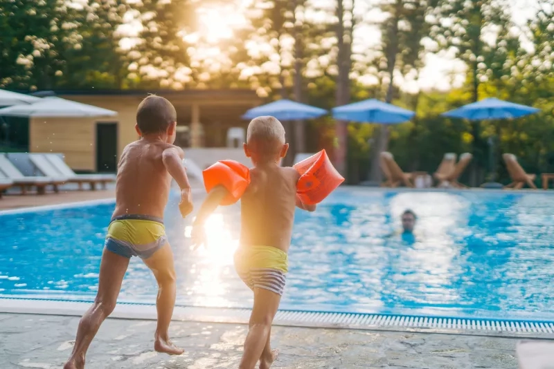 wo boys are jumping into the pool while their dad waits in the pool
