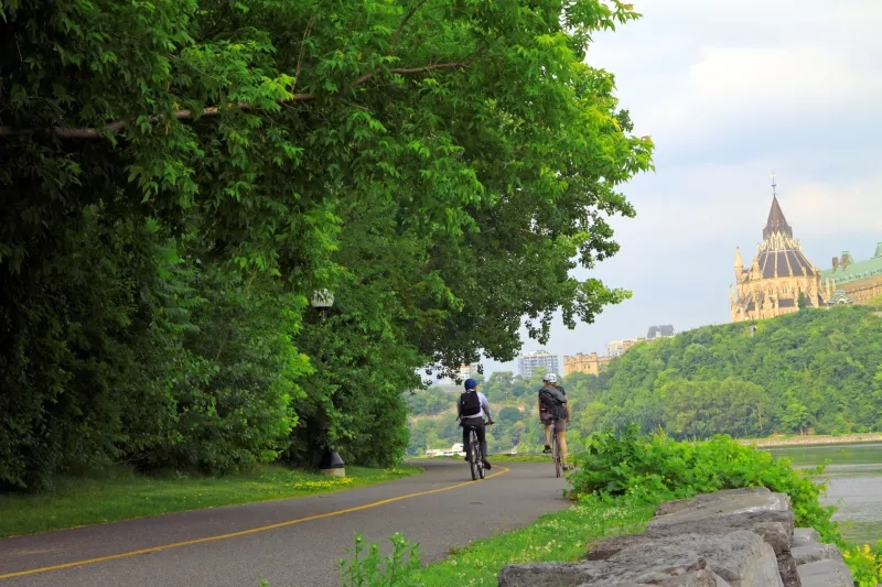 wo cyclists riding along the scenic cycling path with Parliament Hill in Ottawa in the background