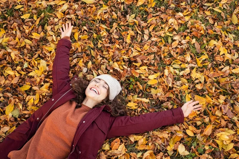 woman lying over autumn leaves with stretched arms 