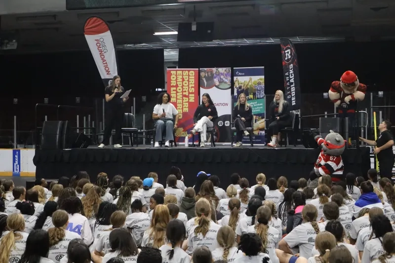 Girls sit facing athletes on a stage for a panel 