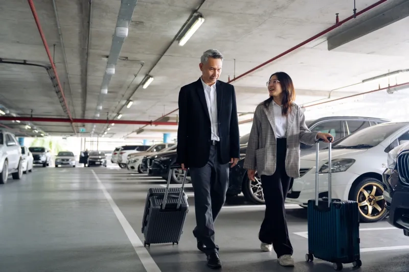 people rolling luggage in an airport parking lot