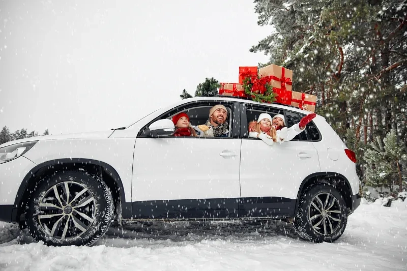 family with children sitting in a car loaded with boxes of gifts and a Christmas tree