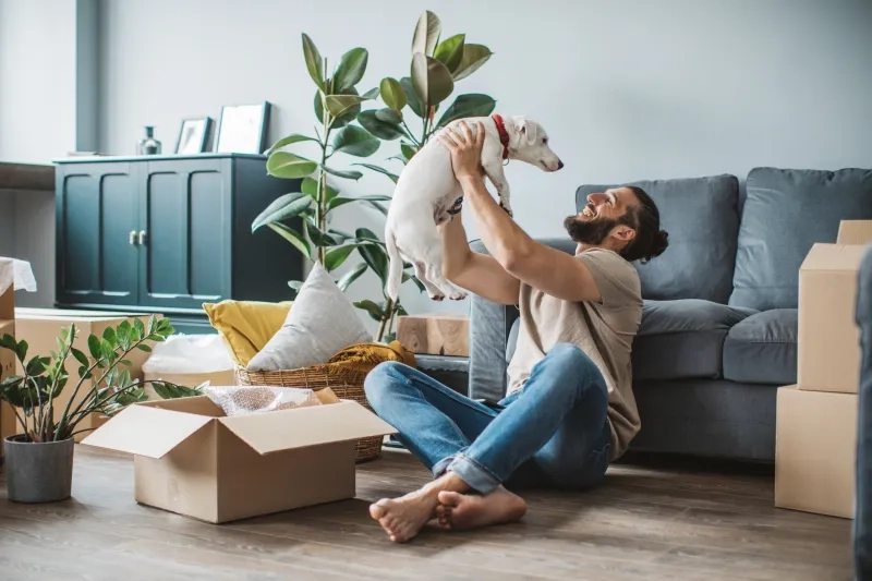 Young men moving in new house. He is happy and playing with his pet dog.