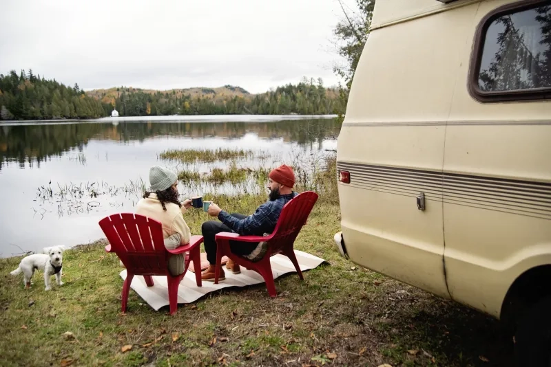 Two people sitting next to RV and a lake