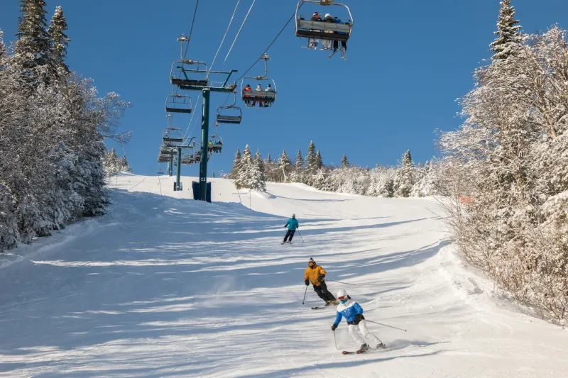 skiers on ski lift with snow covered mountains