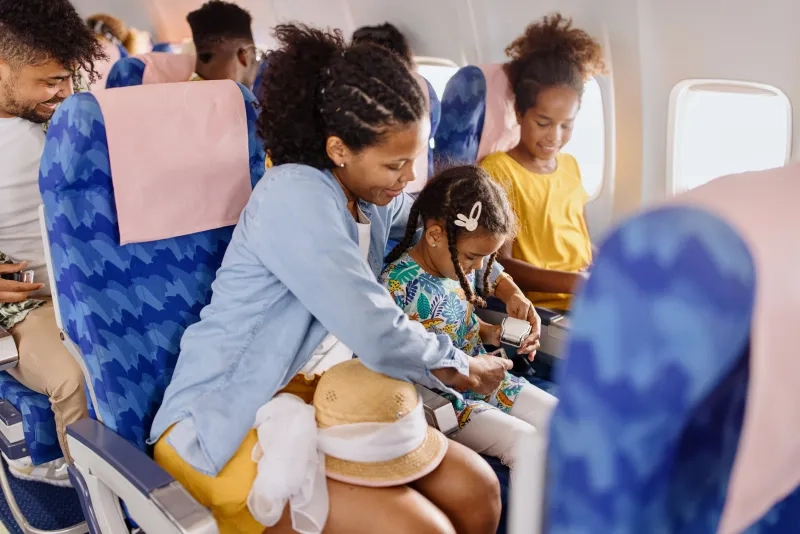 mother helps the child to fasten seat belt on the plane