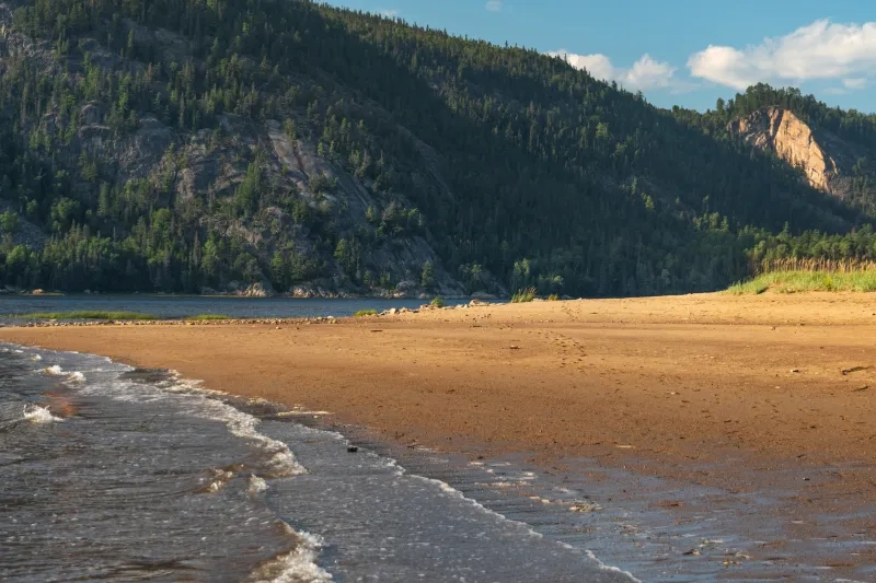 Golden sand beach and forested mountains along the scenic Saguenay fjord