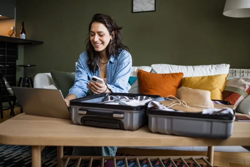 woman packing suitcase and looking at laptop