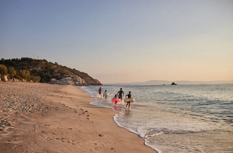 Family running and playing in the shallow water at the beach during summer sunset