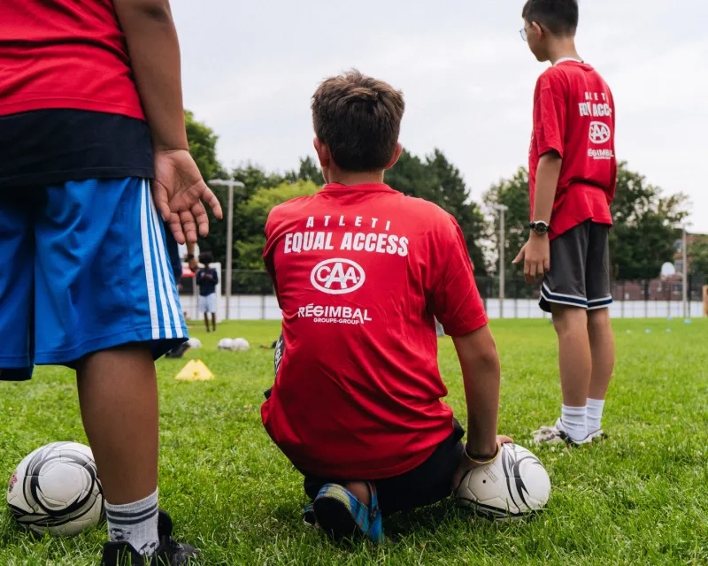 Youth soccer player crouching on a soccer ball.