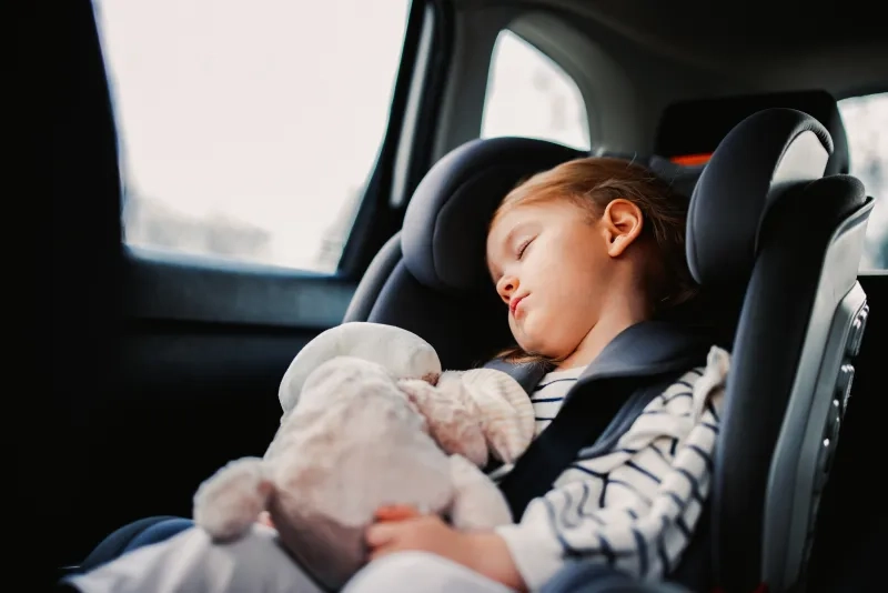 girl napping with her toy in child safety seat in the car