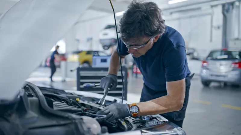 Male Mechanic With Socket Wrench Working On Car Engine In Auto Repair Shop