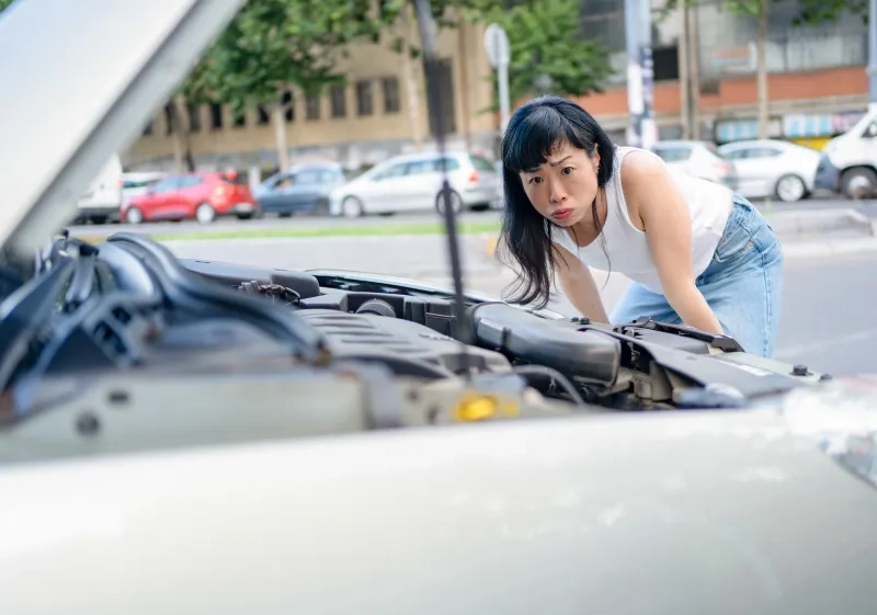 Woman looking at car engine having breakdown on street 