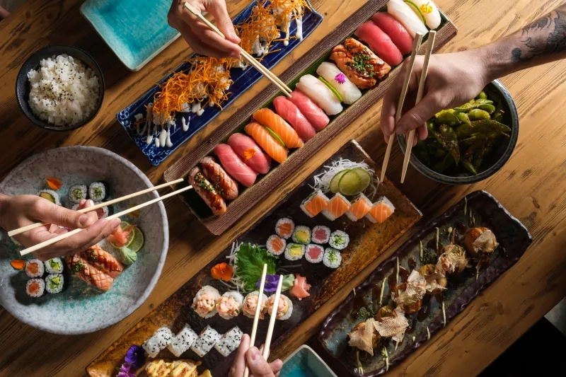 group of friends eating fresh sushi with chopsticks