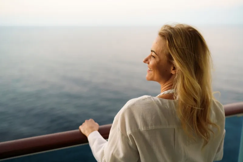 Rear view of happy blonde woman looks at the sea from the terrace of the ship
