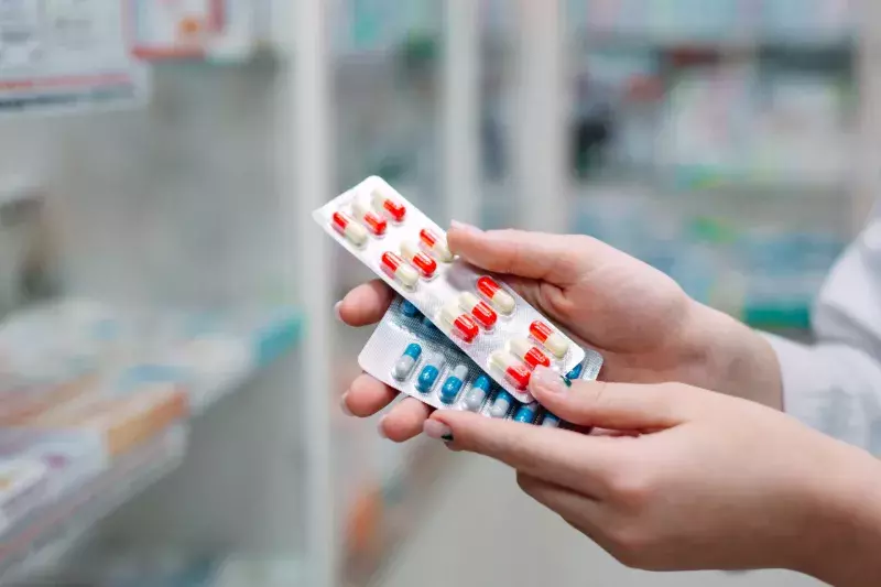 Pharmacist holding medicine box and capsule packs in pharmacy drugstore.